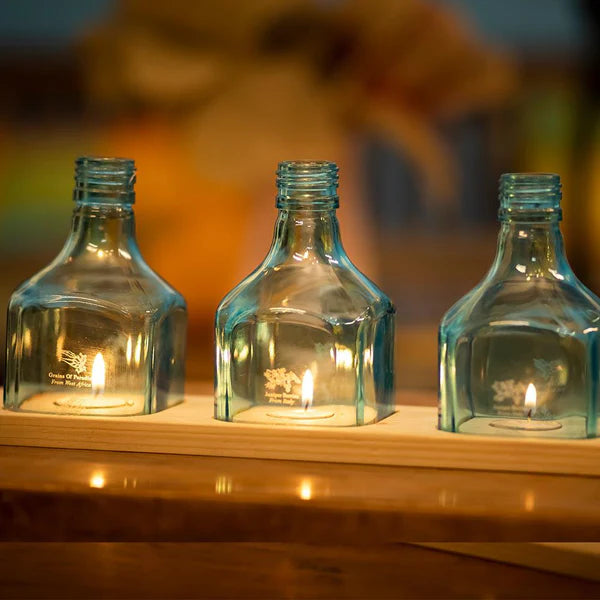 Three glass bottles with lit candles inside on a wooden surface.